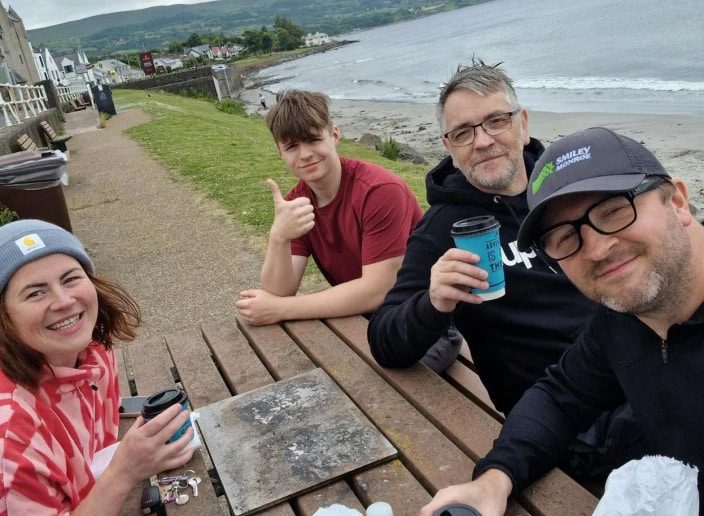 Selfie of four people smiling with coffees while by the sea